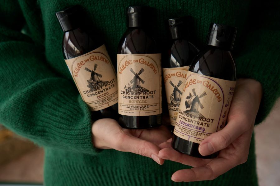 a woman holding four bottles of Vallee de Galene chicory coffee concentrate in her hands against a green sweater