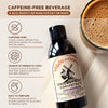 A bottle of Vallee de Galene Chicory Root concentrate with Elderberry is laying on a table next to glass with foamy chicory beverage.