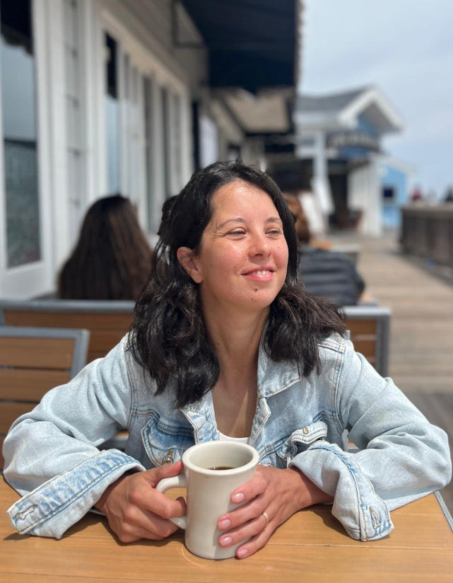 Halina, founder of Vallee de Galene, peacefully enjoying a warm mug of caffeine-free chicory coffee alternative at an outdoor boardwalk table